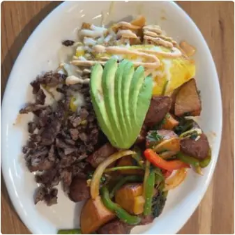 A breakfast plate with an omelet drizzled in sauce, a fanned sliced avocado, chopped grilled steak, and house potatoes with peppers and onions.